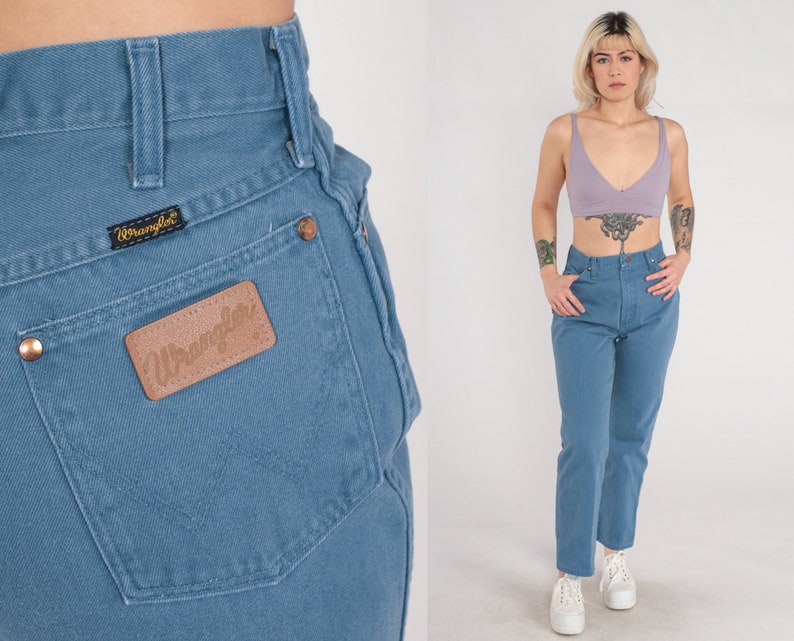 Op de afbeelding: Een lichtblauwe spijkerbroek met een hoge taille en een rechte pijp. De broek heeft een bruin leren patch op de achterzak met het woord "Wrangler" erop gedrukt.
