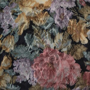 May include: Close-up of a floral fabric with a black background. The pattern features large, textured flowers in shades of pink, purple, gold, and green. The fabric has a woven appearance.