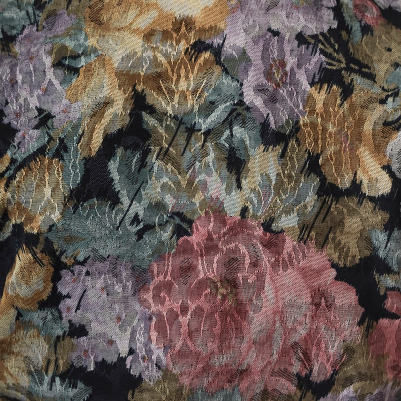 May include: Close-up of a floral fabric with a black background. The pattern features large, textured flowers in shades of pink, purple, gold, and green. The fabric has a woven appearance.