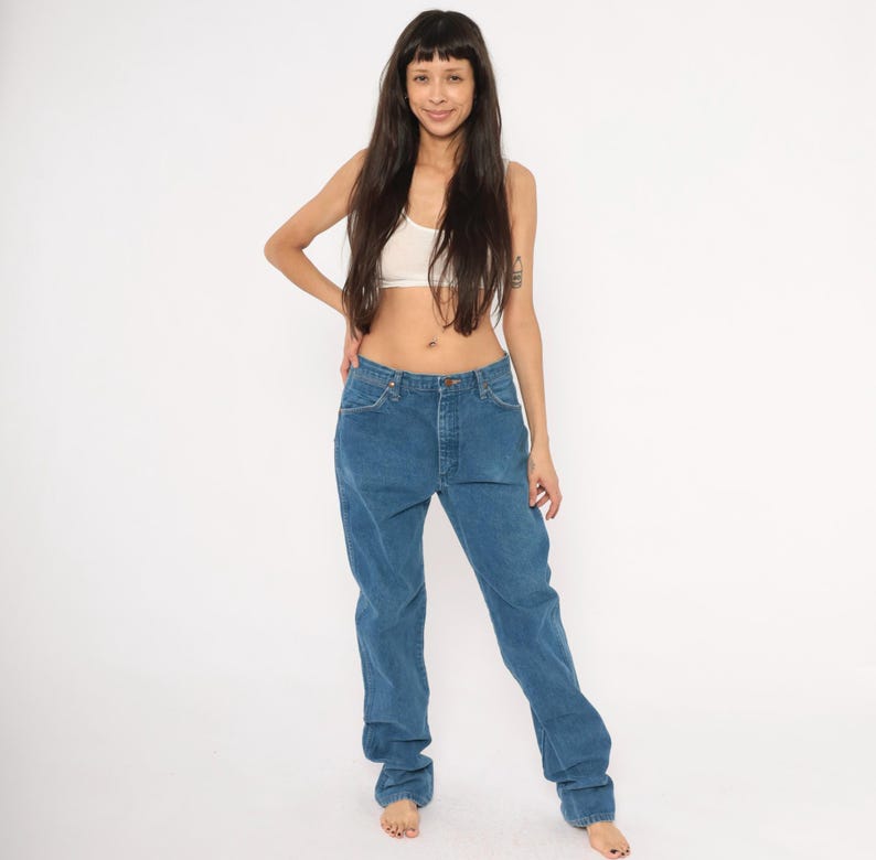 May include: Blue denim jeans with a classic straight leg fit. The jeans have a button and zipper closure and five-pocket styling. The denim is a medium wash, and the jeans appear to be vintage.