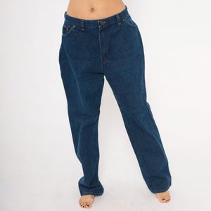 May include: Dark blue denim jeans with a classic five-pocket design. The jeans have a straight leg cut and a button and zipper closure. The denim appears to be a medium weight, suitable for everyday wear. The jeans are shown against a white background.