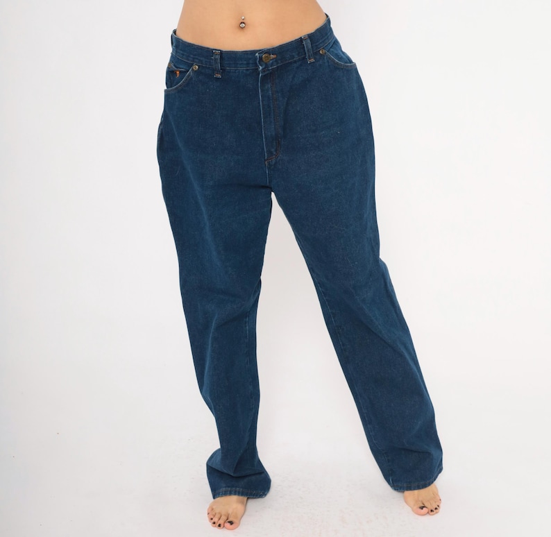 May include: Dark blue denim jeans with a classic five-pocket design. The jeans have a straight leg cut and a button and zipper closure. The denim appears to be a medium weight, suitable for everyday wear. The jeans are shown against a white background.