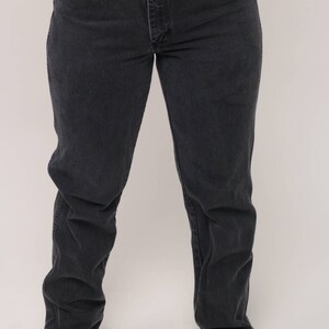May include: Dark wash denim jeans with a straight leg fit. The jeans have a classic five-pocket design, a button and zipper closure, and a contrasting blue pocket detail. The jeans are worn by a person.