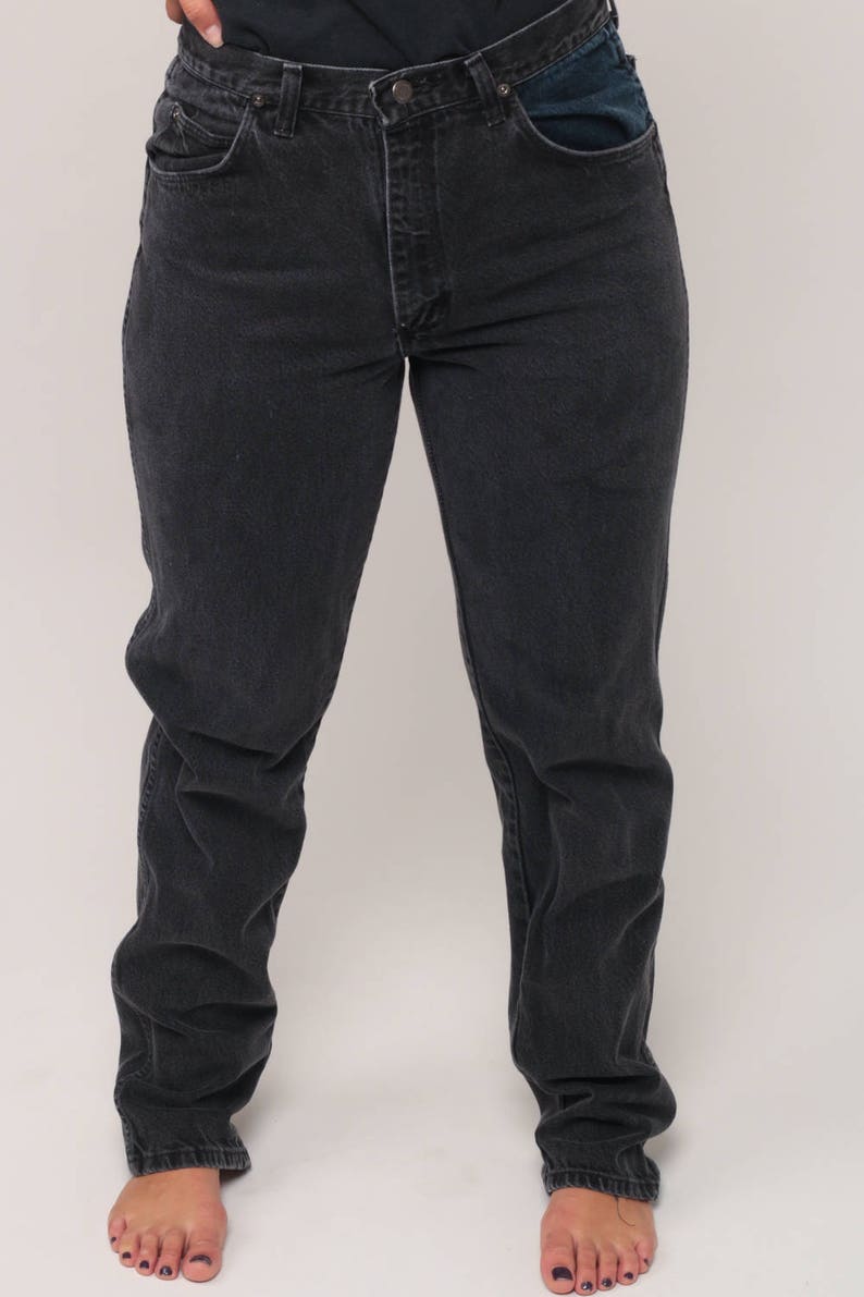 May include: Dark wash denim jeans with a straight leg fit. The jeans have a classic five-pocket design, a button and zipper closure, and a contrasting blue pocket detail. The jeans are worn by a person.