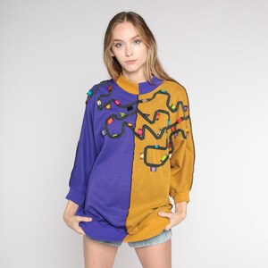 May include: A purple and gold sweatshirt with a colourful abstract design. The design features a black outline and colourful accents.