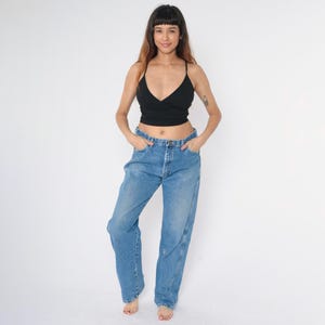 Pu&ograve; includere: Una persona indossa un top corto nero e jeans di denim blu. I jeans hanno una vestibilit&agrave; rilassata e una gamba dritta.