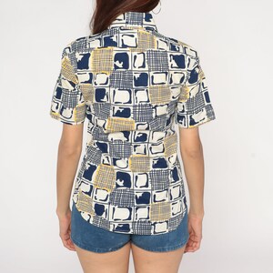May include: A white short-sleeved button-down shirt with a geometric pattern in shades of blue and yellow.
