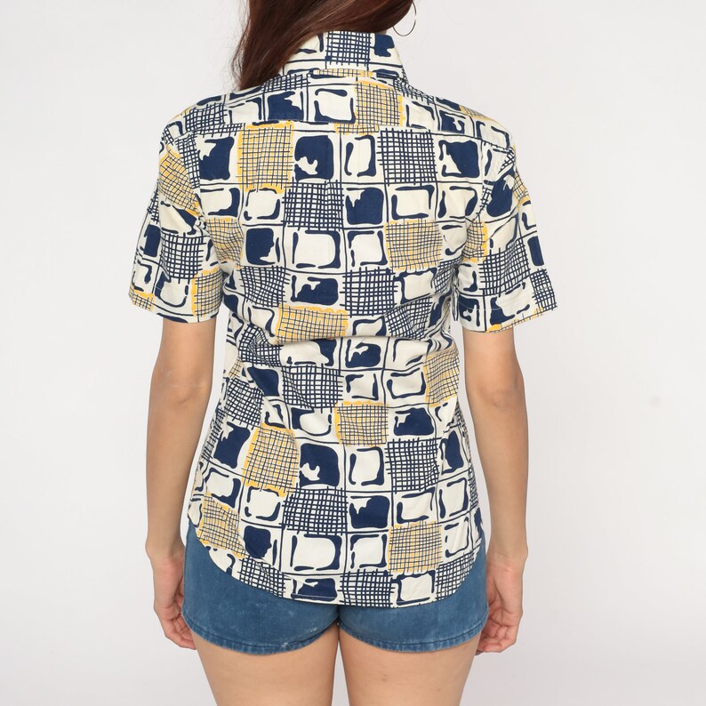 May include: A white short-sleeved button-down shirt with a geometric pattern in shades of blue and yellow.