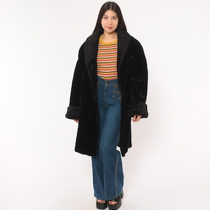 May include: A black coat with a wide collar and long sleeves, worn over a short-sleeved shirt featuring horizontal stripes in yellow, orange, red, green, and blue, paired with high-waisted blue denim flare jeans and black platform sandals.