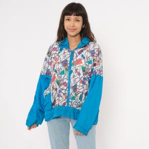 May include: A vintage zip-up jacket with a colorful pattern and bright blue sleeves. The jacket features a white base with a repeating design of chains and colorful shapes. The sleeves and collar are a solid bright blue color.