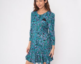 Könnte beinhalten: Ein blaues Kleid mit floralem Muster mit rosa und schwarzen Rosen. Das Kleid hat einen runden Ausschnitt und lange Ärmel.