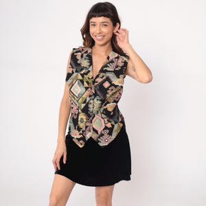 Könnte beinhalten: Eine schwarze Weste mit einem farbenfrohen geometrischen Muster in Rosa, Grün und Gelb. Die Weste hat einen V-Ausschnitt und wird mit einem schwarzen Rock kombiniert. Der Gesamtstil ist vintage und auffällig.