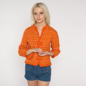 May include: A bright orange and green patterned cardigan with a button closure. The cardigan is made of a soft, fuzzy material.