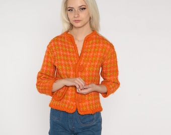 May include: A bright orange and green patterned cardigan with a button closure. The cardigan is made of a soft, fuzzy material.