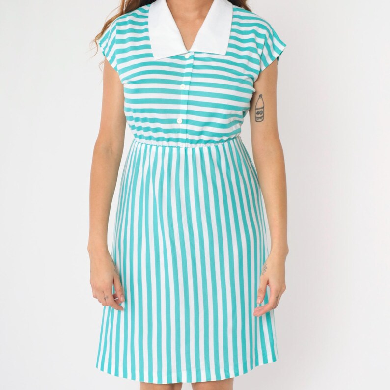 May include: A short-sleeved, white and turquoise striped dress with a white collar and button closure.