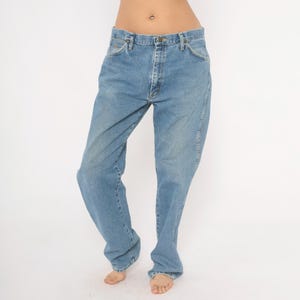 Peut inclure: Jean en denim bleu clair. Le jean a une conception classique &agrave; cinq poches, une fermeture &agrave; bouton et fermeture &eacute;clair, et une coupe droite. Le denim a un aspect d&eacute;lav&eacute;, sugg&eacute;rant l'usure et le lavage.
