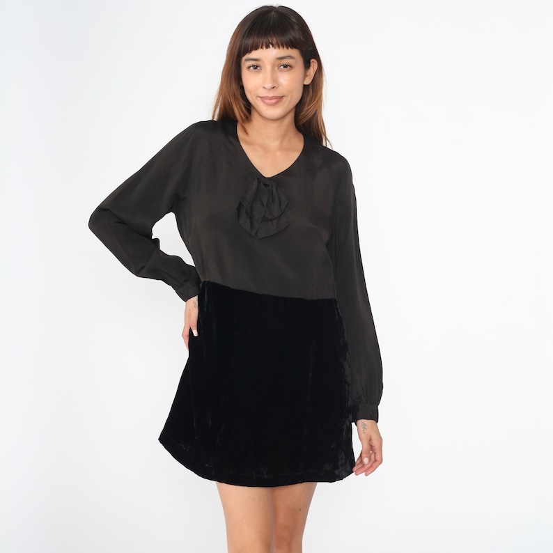 May include: A black velvet mini skirt with a black satin top featuring a bow detail at the neckline.