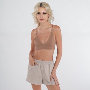 May include: A brown ribbed bralette with a V-neckline and adjustable straps. The bralette is paired with beige, high-waisted, drawstring shorts.