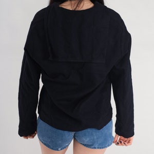 May include: A black long-sleeved shirt with a large, folded collar. The shirt has a relaxed fit and is made of a soft, comfortable fabric.