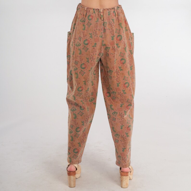 K&ouml;nnte beinhalten: Hoch taillierte Hose in einem gedeckten Braunton mit einem Allover-Druck aus kleinen geometrischen Formen, Sonnen und kreisf&ouml;rmigen Motiven in Gr&uuml;n- und Rott&ouml;nen. Diese Hose hat einen elastischen Bund, Seitentaschen und einen schmal zulaufenden Beinschnitt.