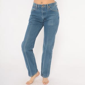 May include: Light blue denim jeans with a classic five-pocket design. The jeans have a straight leg cut and a button and zipper closure. The denim is a medium wash, and the jeans appear to be vintage.