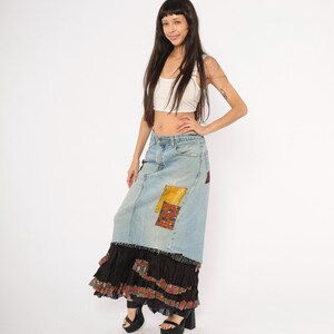 May include: A light blue denim skirt with patchwork details and a black ruffled hem. The skirt has a high waist and a long, flowing silhouette. The patchwork includes yellow and patterned fabric.