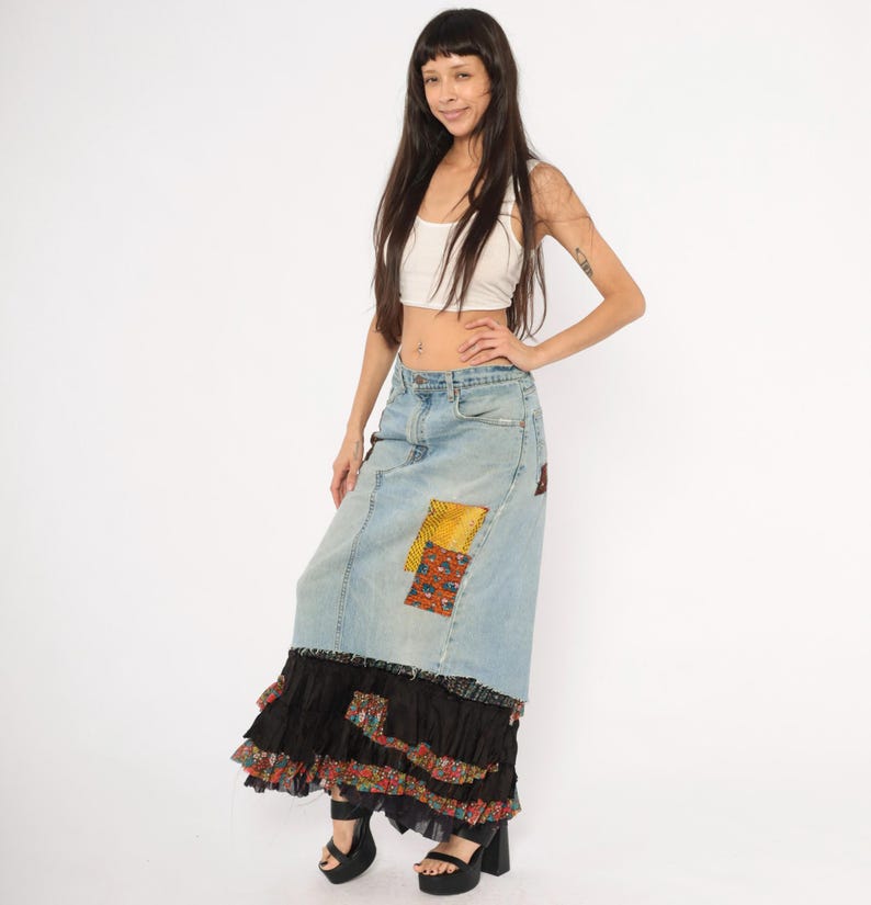 May include: A light blue denim skirt with patchwork details and a black ruffled hem. The skirt has a high waist and a long, flowing silhouette. The patchwork includes yellow and patterned fabric.