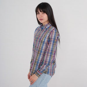 Pode incluir: Uma camisa de xadrez de manga comprida com um esquema de cores azul, vermelho, verde e marrom. A camisa tem um colarinho abotoado e um caimento relaxado.