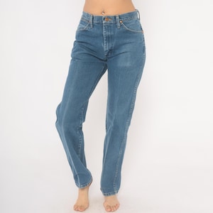 May include: Blue denim jeans with a classic straight leg fit. The jeans have a button and zipper closure, with pockets in the front and back. The denim is a medium wash, and the jeans appear to be vintage.