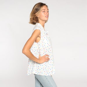 May include: White sleeveless collared shirt with a colorful confetti pattern. The shirt has a button-down front and a relaxed fit. The model is wearing light blue jeans. The shirt is made of a lightweight fabric.