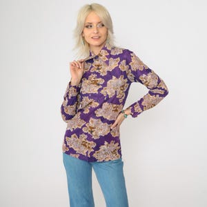 May include: A purple long-sleeved shirt with a brown floral print. The shirt has a collared neckline and button closure.
