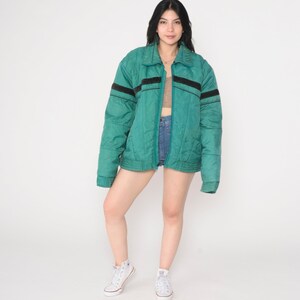 May include: A teal blue quilted jacket with black stripes on the sleeves and a zipper closure.