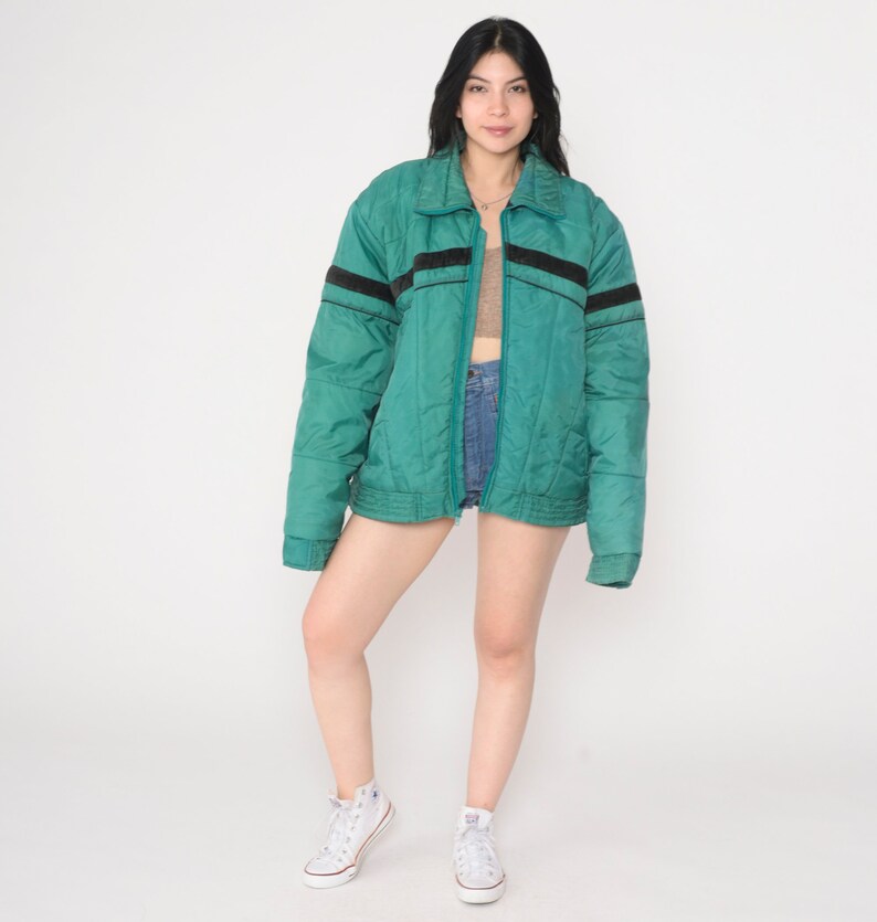 May include: A teal blue quilted jacket with black stripes on the sleeves and a zipper closure.