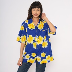 May include: A blue button-down shirt with a vibrant yellow hibiscus flower pattern. The short-sleeved shirt has a classic collar and a chest pocket. The floral print is repeated across the fabric.