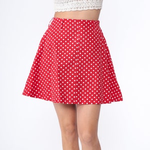 Peut inclure: Une jupe rouge &agrave; pois blancs. La jupe est trap&egrave;ze et a une taille haute.