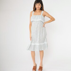 May include: A white midi dress with a floral print and lace trim. The dress has a square neckline and thin straps.