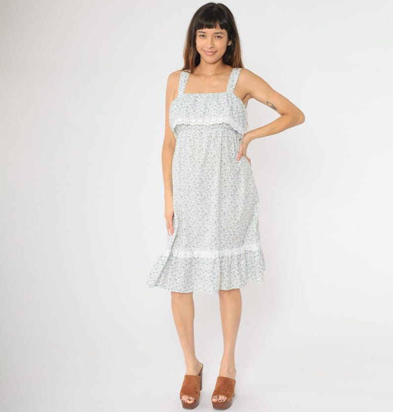May include: A white midi dress with a floral print and lace trim. The dress has a square neckline and thin straps.