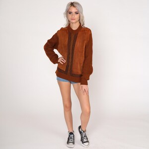 May include: A brown sweater with a suede panel and cable knit detail. The sweater has a round neckline and long sleeves.