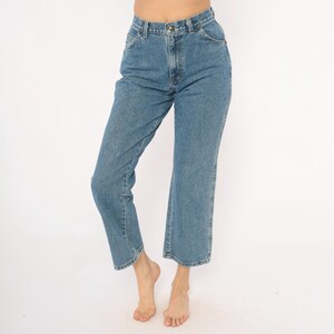 May include: Light blue denim jeans with a classic five-pocket design. The jeans have a straight leg cut that ends just above the ankles. The jeans are made of a sturdy denim material and feature a button and zipper closure.