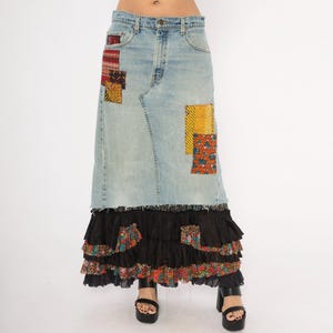 May include: Light wash denim skirt with patchwork details and a tiered black ruffle hem. The skirt features colourful fabric patches in red, yellow, and orange. The skirt is worn with black platform sandals.