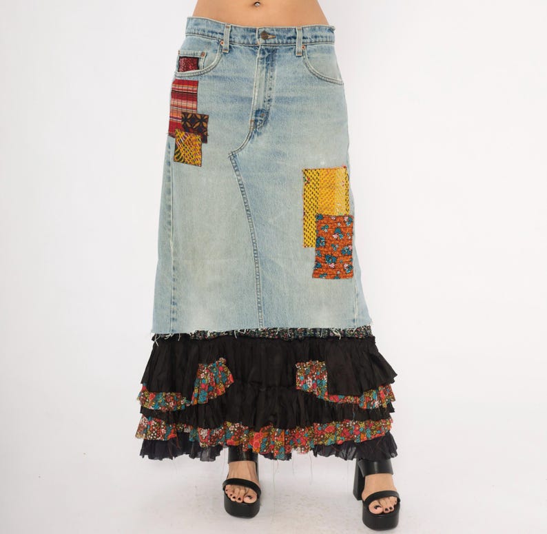May include: Light wash denim skirt with patchwork details and a tiered black ruffle hem. The skirt features colourful fabric patches in red, yellow, and orange. The skirt is worn with black platform sandals.