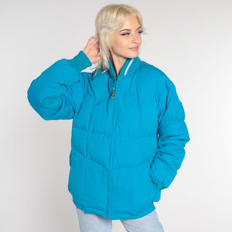 May include: A bright turquoise blue puffer jacket with a zipper closure and a white stripe on the collar.