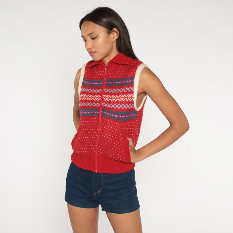 May include: Red sleeveless knitted vest with a white collar and a zip down the front. The vest has a geometric pattern in blue, white and pink.