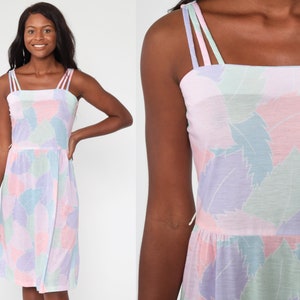 May include: A sleeveless dress with a pastel pink, purple, and green abstract leaf pattern. The dress has a square neckline and thin straps.