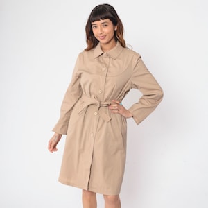 May include: A beige trench coat with a button-up front and a belt. The coat has long sleeves and a collared neckline.