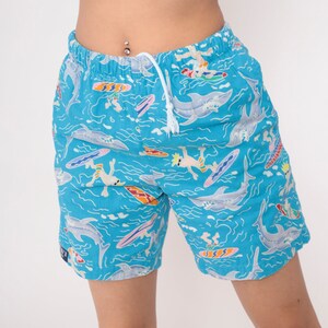 K&ouml;nnte beinhalten: Blaue Badehose mit einem bunten Druck von Haien, Surfern und Wellen.