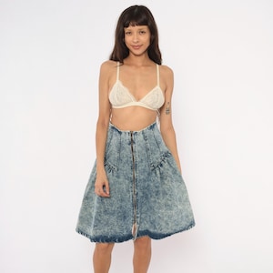 May include: A high-waisted acid wash denim skirt featuring a full, flared silhouette and a prominent center front zipper closure. The skirt has a distinct mottled blue and white texture, structured seams at the waist, and a knee-length hemline.