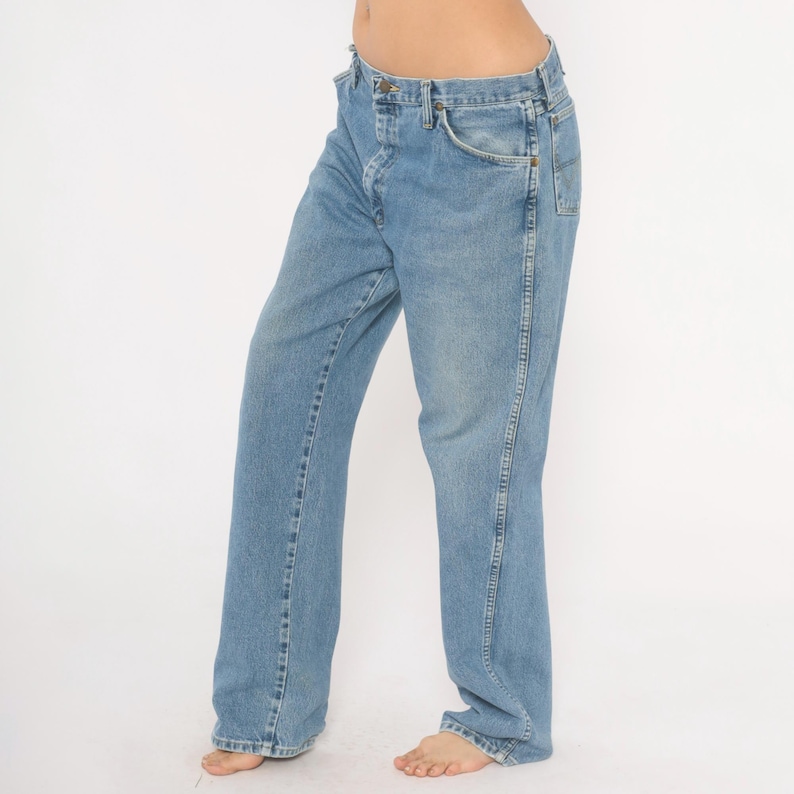 Peut inclure: Jean en denim bleu clair avec une conception classique &agrave; cinq poches. Le jean a une coupe droite et une fermeture &agrave; bouton et &agrave; glissi&egrave;re. Le denim a un d&eacute;lavage d&eacute;color&eacute;, lui donnant un aspect vintage. Le jean est port&eacute; par une personne.