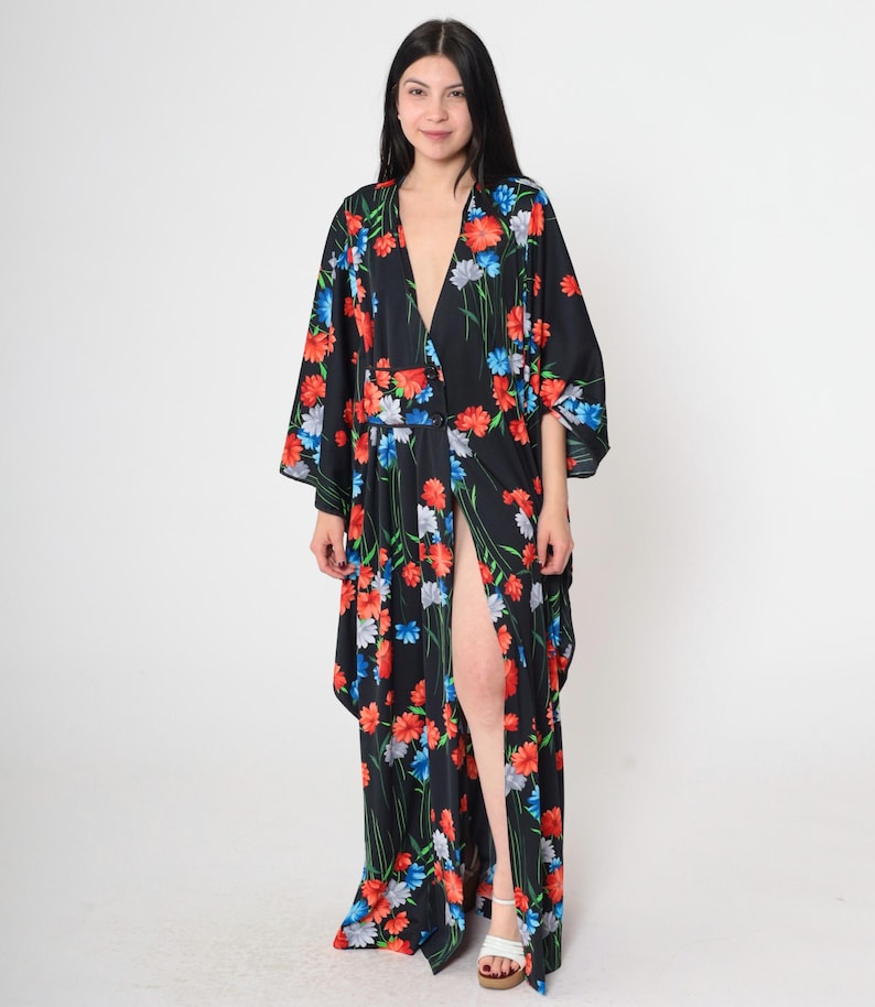 May include: A long black maxi dress with a floral print in shades of red, blue, and white. The dress has a deep V-neckline, a front slit, and long sleeves.