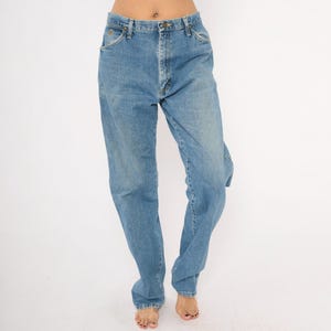 Pu&ograve; includere: Jeans di denim blu chiaro con un classico design a cinque tasche. I jeans hanno una vestibilit&agrave; a gamba dritta e una chiusura con bottoni e cerniera. Il denim ha un lavaggio sbiadito, che conferisce loro un aspetto vintage. I jeans sono indossati da una persona.